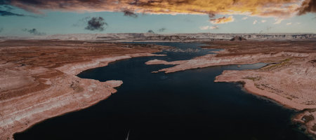 A river flows through a desert landscape with a dark blue river and brown sandy banks under a cloudy...