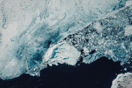 Aerial view of a landmass covered in ice and snow, with a large body of dark water visible below.
