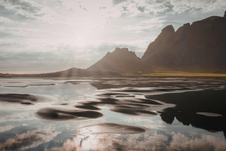 A serene landscape featuring a mountain range reflected in a body of water during sunset.