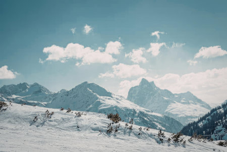 A serene snowy mountain landscape with a clear blue sky and white clouds, featuring snow-covered...