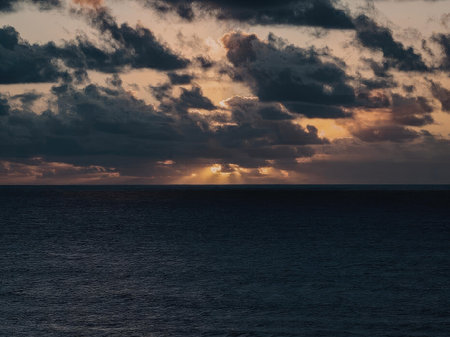 A serene sunset over the ocean with clouds illuminated by the setting sun.