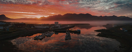 A breathtaking sunset over a calm lake with boats and a majestic mountain range in the background.の写真素材