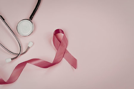 A stethoscope placed alongside a pink ribbon on a soft pink background, symbolizing support for...