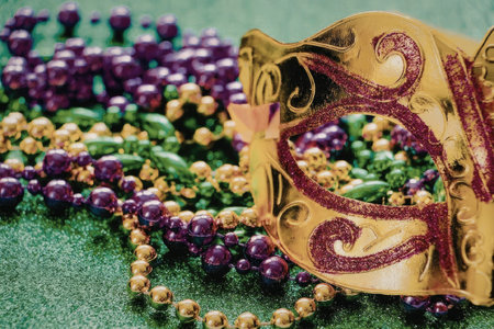 A colorful arrangement of Mardi Gras beads and a decorative mask on a green surface.