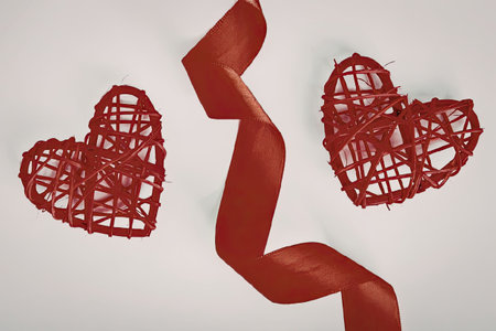 Two red heart-shaped objects made of woven material are placed on either side of a curled red ribbon...