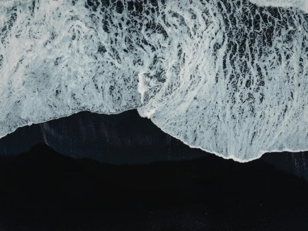 A close-up view of a wave crashing on a dark shore, highlighting the white foam and water texture.の写真素材