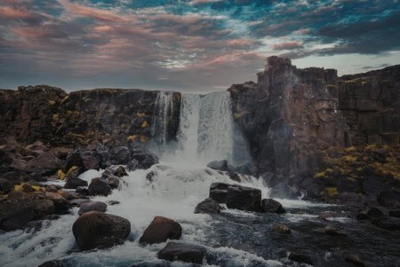 a waterfall flowing through a rocky landscape during a colorful sunset