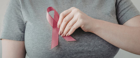 A woman wearing a pink ribbon on her grey t-shirt to show support for breast cancer awareness.