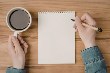 A person is sitting at a wooden desk, holding a cup of coffee in one hand and a pencil in the other,...
