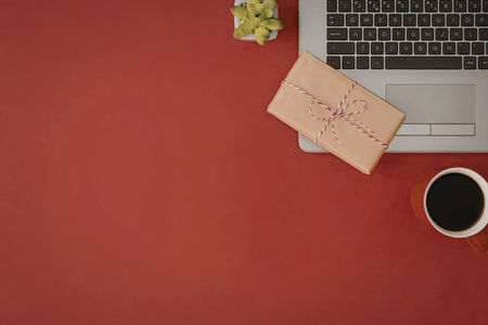 A laptop, a cup of coffee, and a gift box on a red surface.