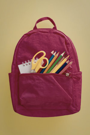 A pink backpack with school supplies, including pencils, scissors, and a notebook, protruding from...