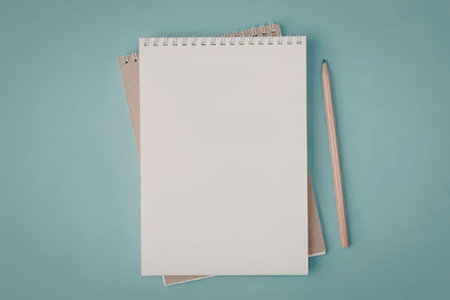 A spiral bound notebook with blank pages, a brown envelope, and a pencil on a light blue background.