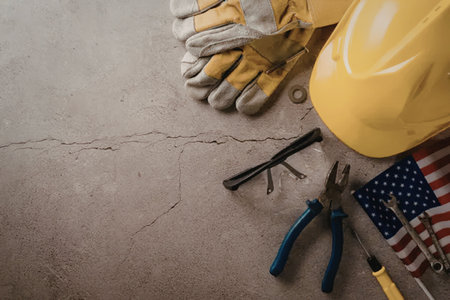 An arrangement of American flag, construction tools and safety gear on a concrete floor