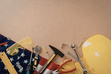 A collection of construction tools and safety gear arranged with an American flag on a brown...