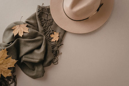 An image of a green scarf with yellow leaves and a beige hat on a neutral background.