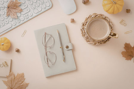 A flat lay of an office desk with autumnal decorations, featuring a notebook, glasses, pen, coffee,...