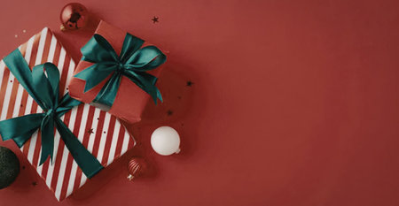 A red and white striped gift box with green ribbon on a red background with Christmas ornaments.