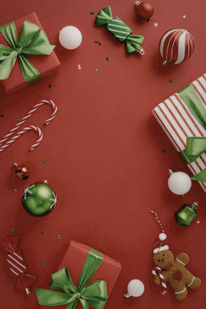 christmas gifts wrapped in red and green with green ribbons and bows surrounded by candy canes, ornaments, and confetti on a red backgroundの写真素材
