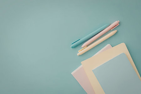 A stack of colorful sticky notes and pens on a blue background, featuring pastel shades of pink,...