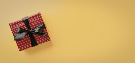 A red gift box with a black ribbon on a bright yellow background