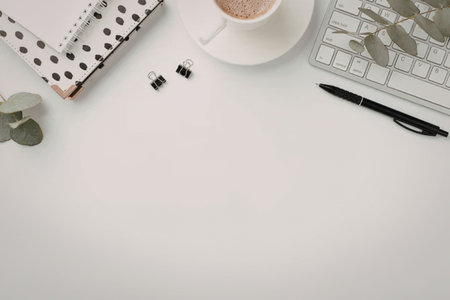 A minimalist workspace featuring a cup of coffee, a notebook, a keyboard, and a pen on a white desk.