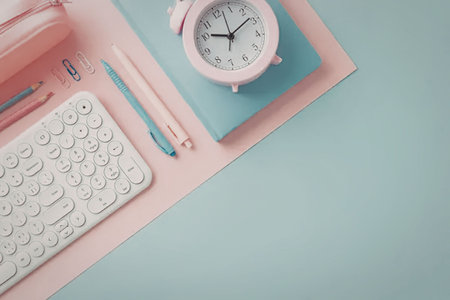 A pastel-colored office desk setup featuring a white keyboard, pink telephone, blue notebook, pink...