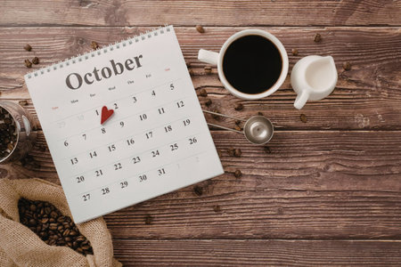 A calendar for October with a cup of coffee, coffee beans, and a wooden table background.
