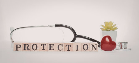 A stethoscope, a red heart, and a small plant are arranged with wooden blocks spelling 'PROTECTION'...