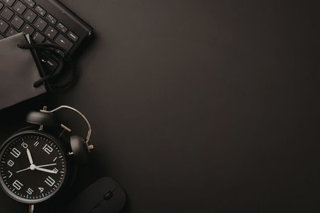 A dark desk with a black alarm clock and keyboard on it