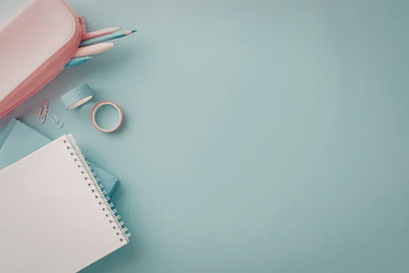 A spiral notebook, pink pencil case with colored pencils, scissors, and paper clips on a light blue...