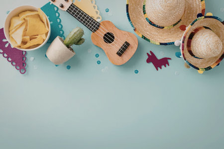 A colorful arrangement of fiesta elements including a ukulele, sombrero, chips, and decorations on a light blue background.の写真素材