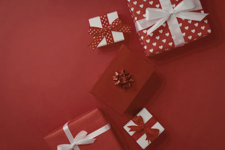 A group of wrapped Christmas presents on a red background, featuring various ribbons and bows.