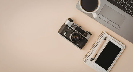 A workspace setup featuring a laptop, coffee cup, camera, spiral notebook, and tablet.