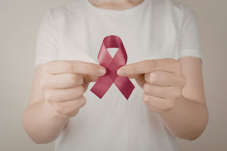 A person wearing a white t-shirt holds a pink breast cancer awareness ribbon between their index...