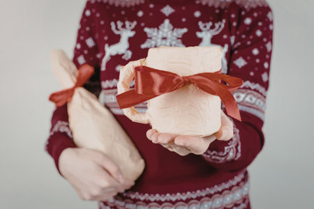 A person wearing a red Christmas sweater with white reindeer and snowflake patterns holds out a...