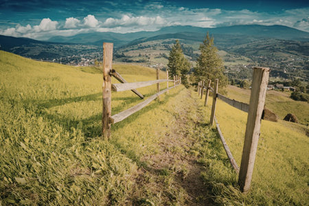 a wooden fence on a green hillside with mountains in the background and a blue sky with clouds
