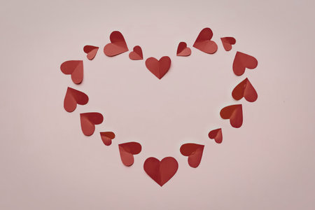 A heart shape made of smaller red hearts on a pink background