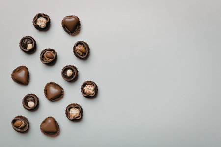 A group of chocolate-covered nuts are scattered on a light surface, some of them cracked open to reveal their inner texture.