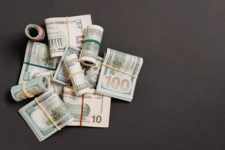 A pile of rolled up banknotes secured with colored bands on a dark gray background.