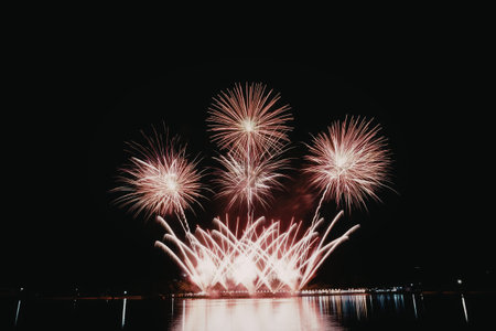 A vibrant fireworks display over a body of water at night, with bursts of pink and orange light reflecting on the surface.の写真素材