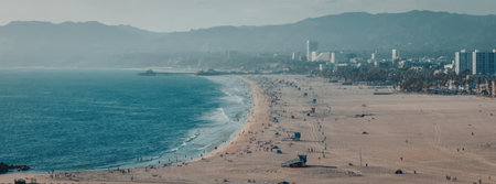 A scenic view of a beach with a city skyline in the background and mountains in the distance.