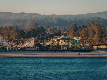 A vibrant amusement park situated on the waterfront, with a stunning backdrop of trees and mountains during sunset.