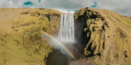 A beautiful waterfall cascading down a lush green mountain with a vibrant rainbow appearing in the mist