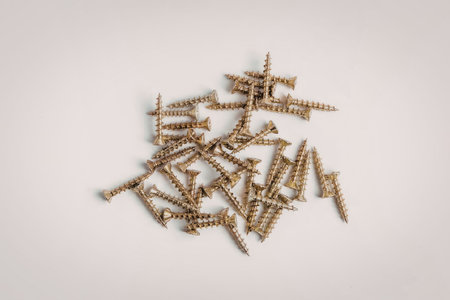 A collection of small brass screws with a Phillips head, scattered on a white background.