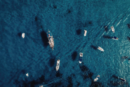 An aerial view of several boats floating on a clear blue body of water, showcasing a serene and peaceful scene.