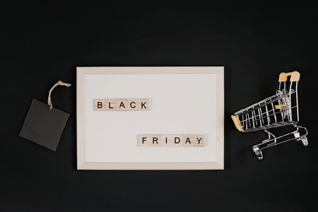 A creative arrangement of a shopping cart, a tag, and a framed 'Black Friday' sign on a black background, symbolizing the shopping sale event.