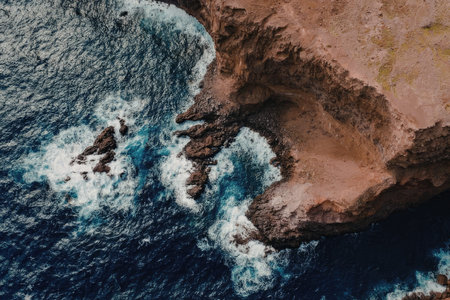 An aerial view of ocean waves crashing against a rocky shore, showcasing the powerful blue waters and rugged terrain.
