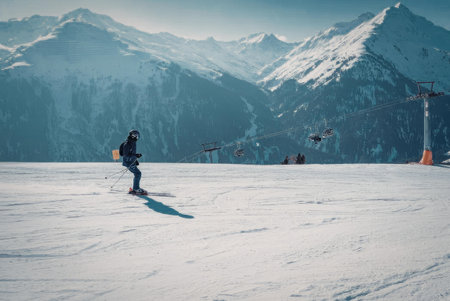 a person skiing down a snowy mountain with a ski lift and mountains in the background