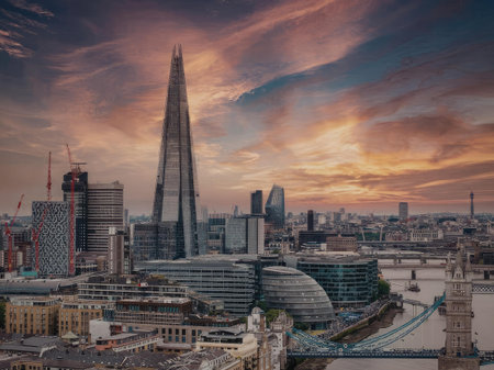 The Shard, a tall glass skyscraper, stands out against a vibrant sunset sky in London. The Thames River runs alongside modern and historic buildings.