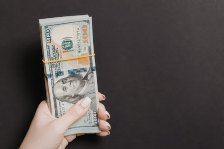 A hand holding a bundle of banknotes secured with a yellow rubber band against a dark background.
